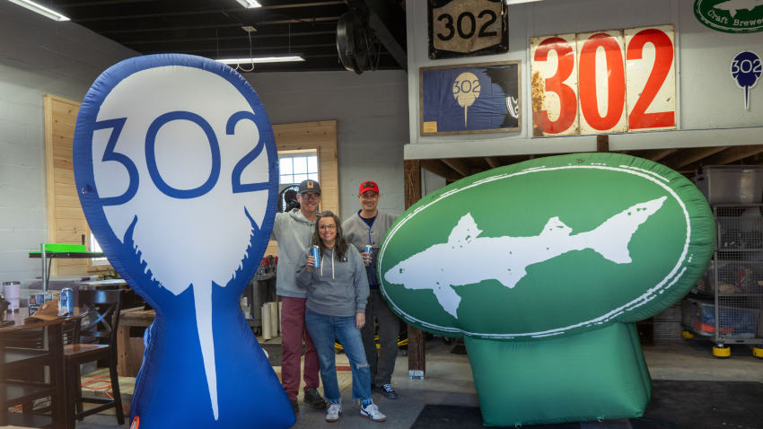 Dogfish Head & 302 Horseshoe Crab Present Third Annual 302 Day, Event Celebrating the Goodness of Delaware 11 On the left, a giant blue inflatable with the 302 Horseshoe Crab logo. On the right, a giant green inflatable with the 302 Dogfish Head logo. 3 people standing in the middle.