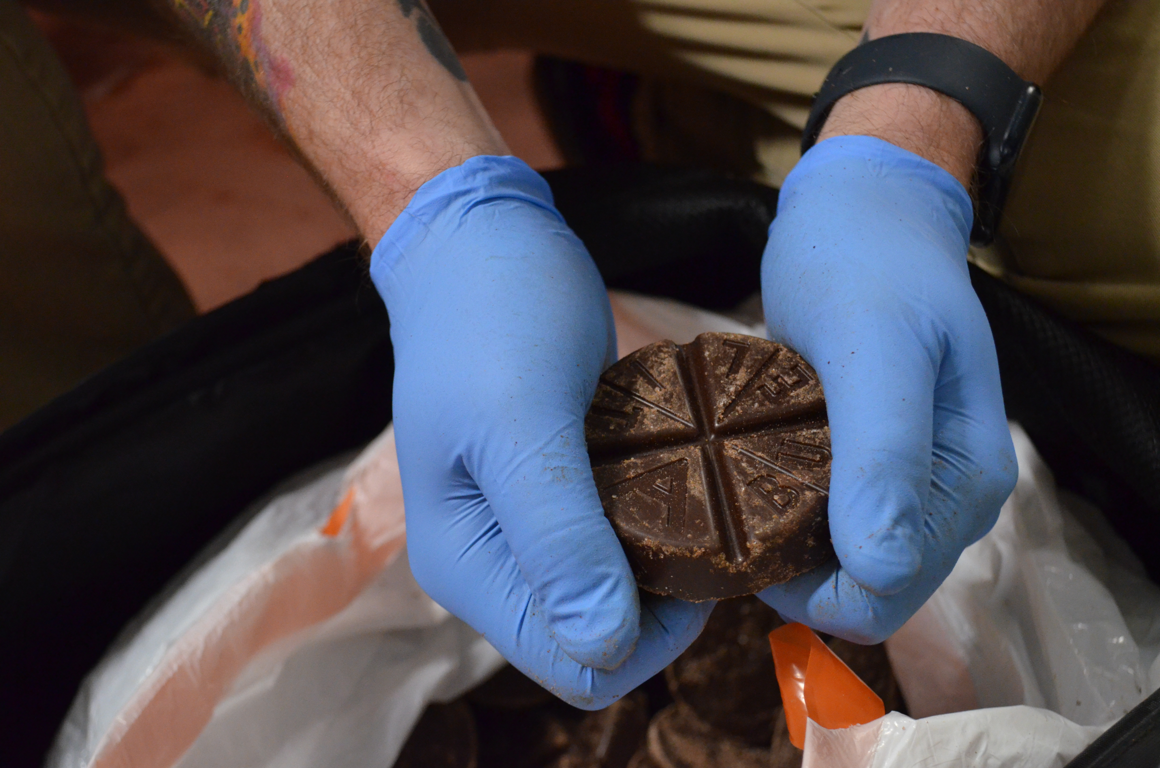 Boulevard Releasing Mexican Xocolatl Ale 20 Person wearing blue gloves holding a round, segmented chocolate disc over a bag filled with similar discs.