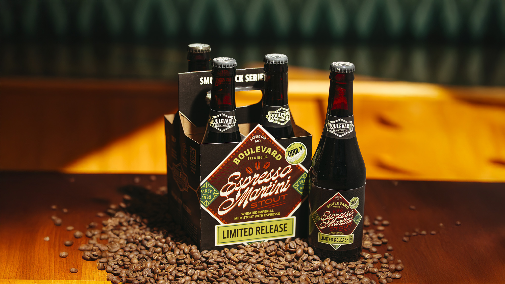Boulevard Releasing Espresso Martini Stout 8 A four-pack of Boulevard Brewing Co.'s Espresso Martini Stout is displayed on a wooden table surrounded by coffee beans. The bottles are dark with labels matching the box, which reads "Limited Release" and features coffee-themed graphics.
