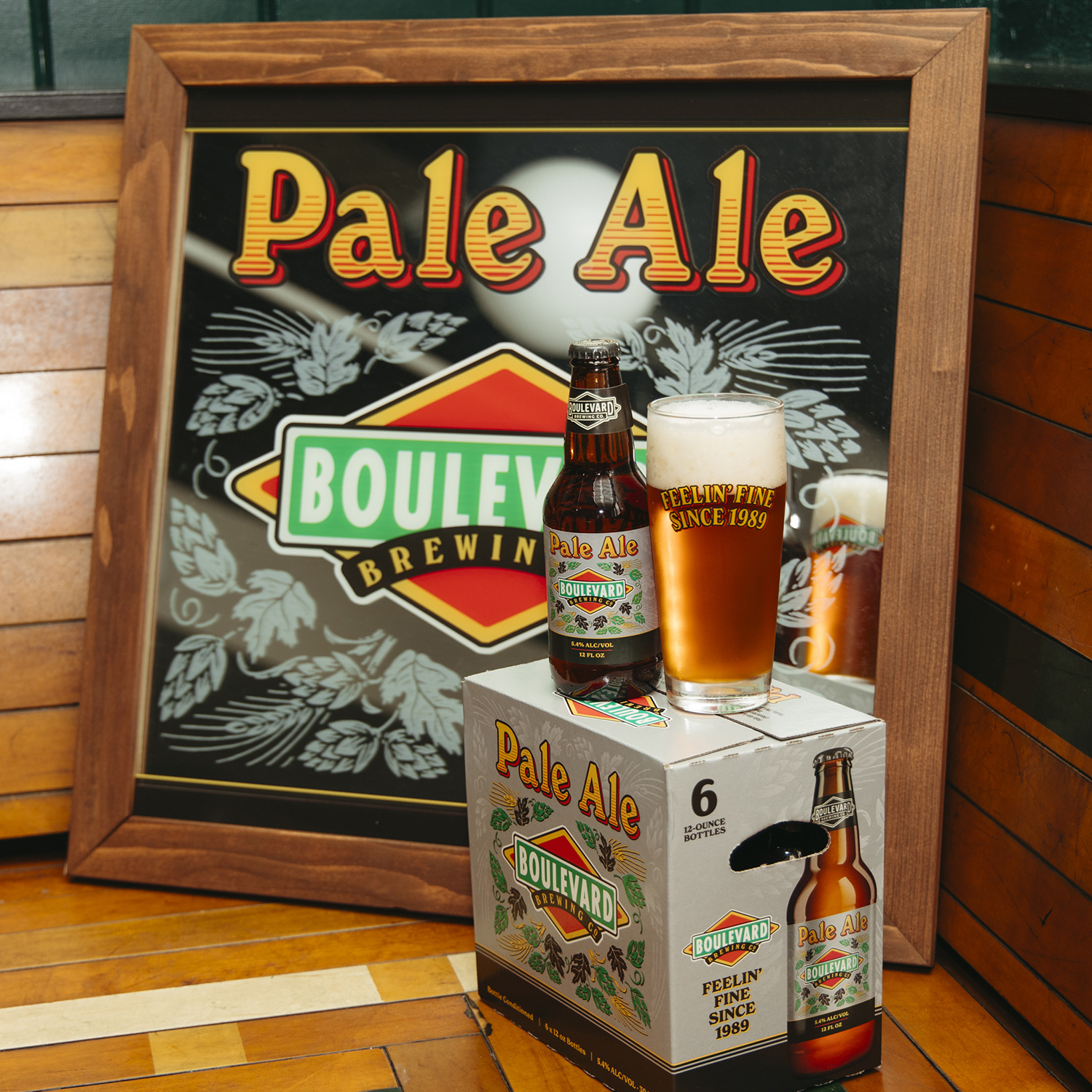 Boulevard Brewing Celebrating 35 Years 38 A bottle of Boulevard Brewing Co. Pale Ale sits next to a filled glass on top of a six-pack box of the same Pale Ale. Behind them is a framed sign featuring the Boulevard Brewing Co. logo and the words "Pale Ale" printed prominently at the top.