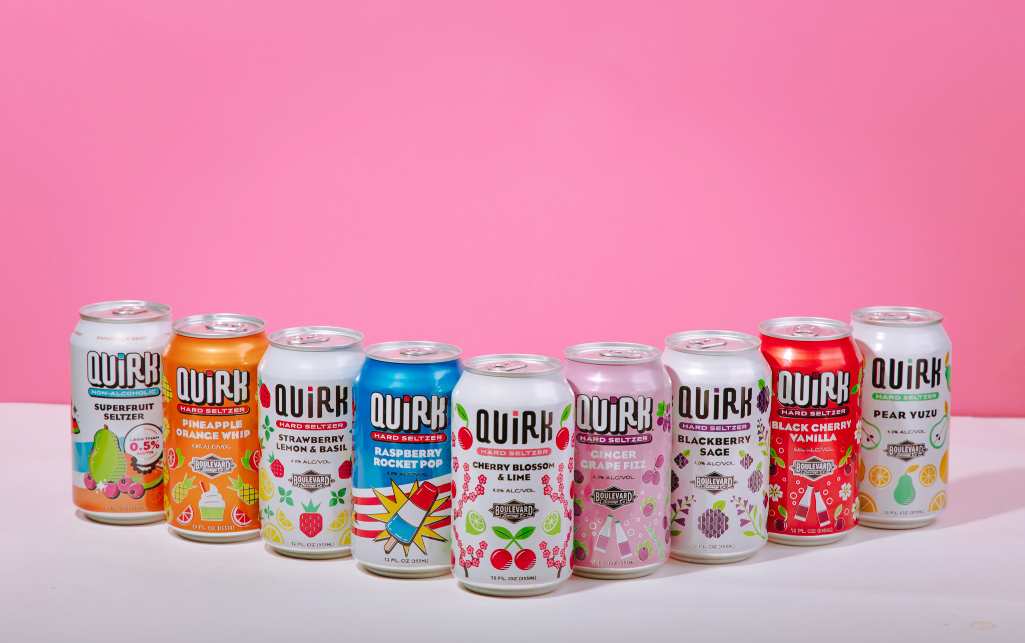 Boulevard Brewing Celebrating 35 Years 33 A row of Quirk Hard Seltzer cans lined up against a pink background. The flavors displayed from left to right include Superberry, Pineapple Orange Whip, Strawberry Lemon Basil, Raspberry Rocket Pop, Cherry Blossom & Lime, Blackberry Sage, Blueberry Lemon & Lavender, Ginger & Hops, Black Cherry & Vanilla, and Pear Yuzu. Each can boasts vibrant designs reflecting its unique flavor