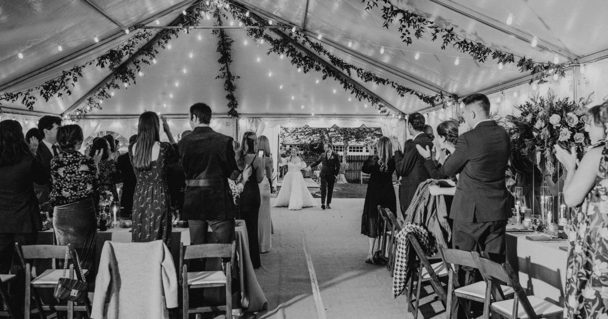 Dogfish Head Weddings - Love is INN the Air 37 a bride and groom entering a tented wedding of guests standing and clapping