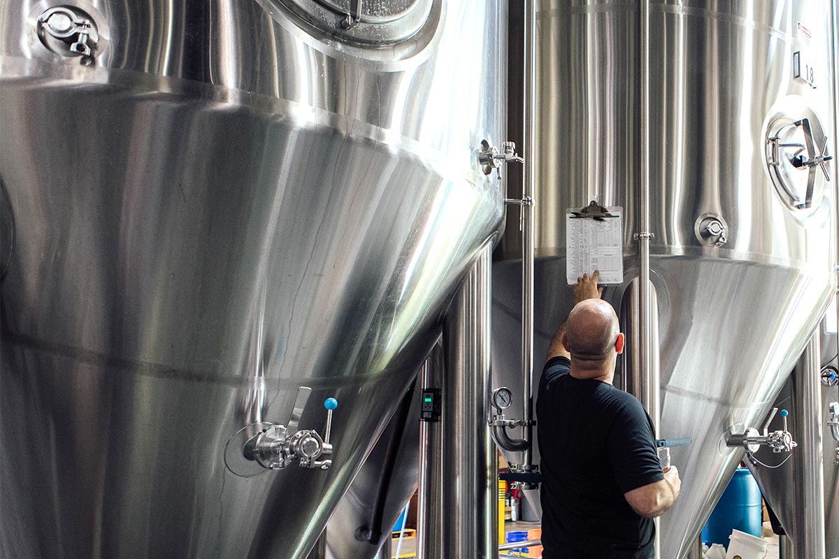Brewers Association: The 2024 Election and Small and Independent Breweries 9 Brewer in front of fermenter tanks looking at beer recipe