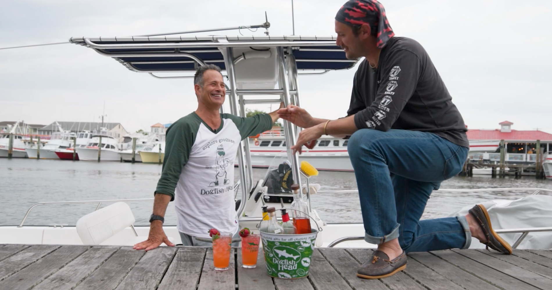 Dogfish Head - The Adventures of Pawpaw Pirate & Captain Strawberry: The Pawberry Cocktail 13 Sam Calagione and brad Leone with two pink cocktails in hurricane glasses on a dock in Lewes, Delaware with the S.S. Dogfish boat in the water behind them