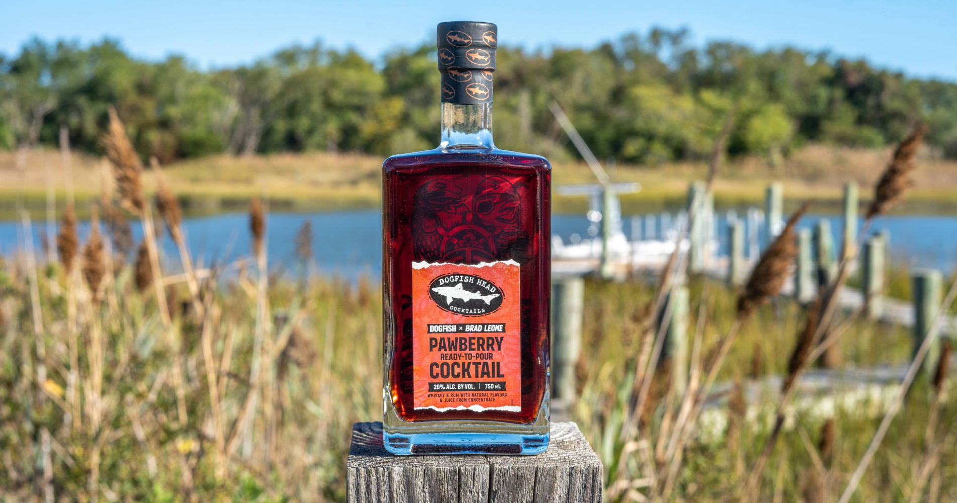 Dogfish Head - The Adventures of Pawpaw Pirate & Captain Strawberry: The Pawberry Cocktail 16 Bottle of Pawberry Ready-To-Pour cocktail on a deck with a boat behind it
