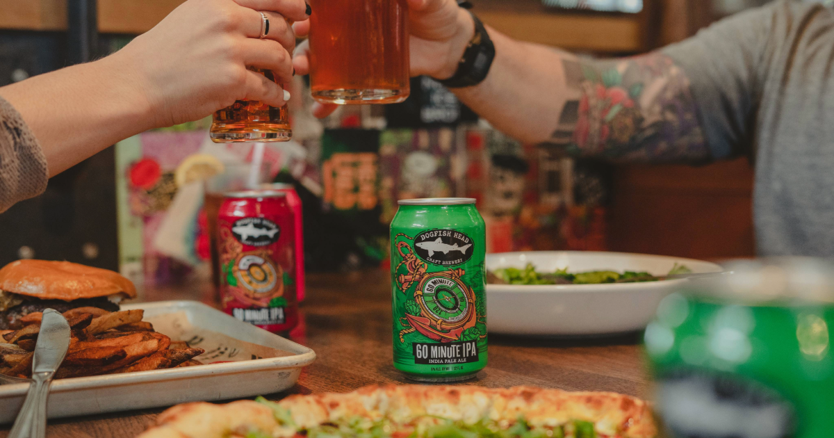 Dogfish Head Adding 30 Minute Light IPA 12 Dogfish Head 60 and 90 Minute IPAs being cheersed with two people at a table with pizza and a cheese burger