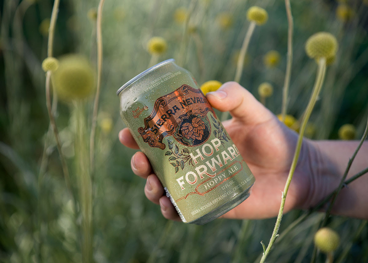 A hand holding a can of Hop Forward, surrounded by garden flowers Sierra Nevada Releasing Hop Forward For Earth Day