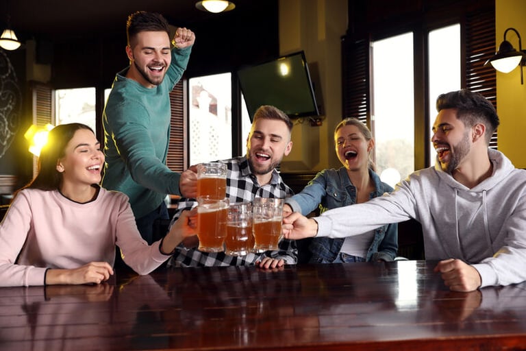 Group of people enjoying drinks, raising beer glasses in a lively bar setting with a friend who doesn’t want to drink beer