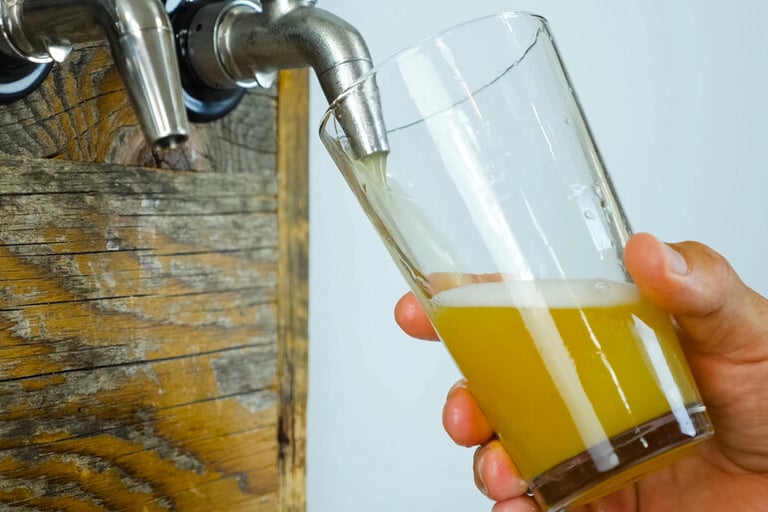 Homebrewer pouring fresh craft beer from a tap into a glass, comparing plastic vs. stainless steel pressure barrels for homebrewing.
