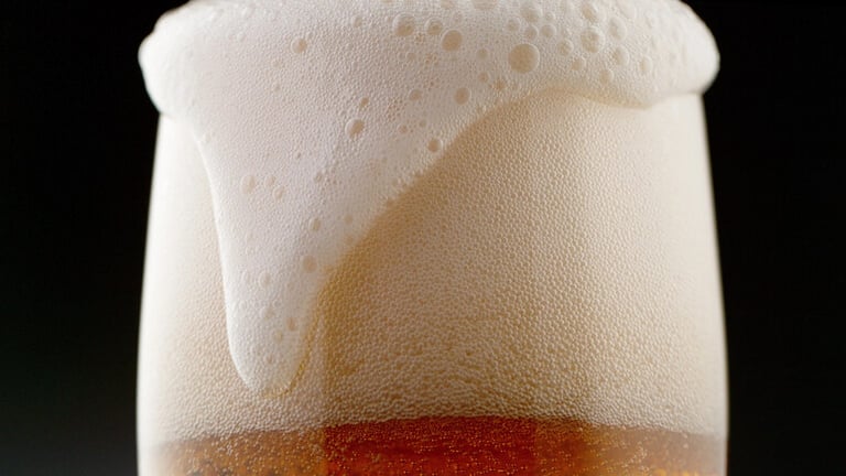 Close-up view of a beer glass with thick creamy foam highlighting nitro beer texture and smooth pour.