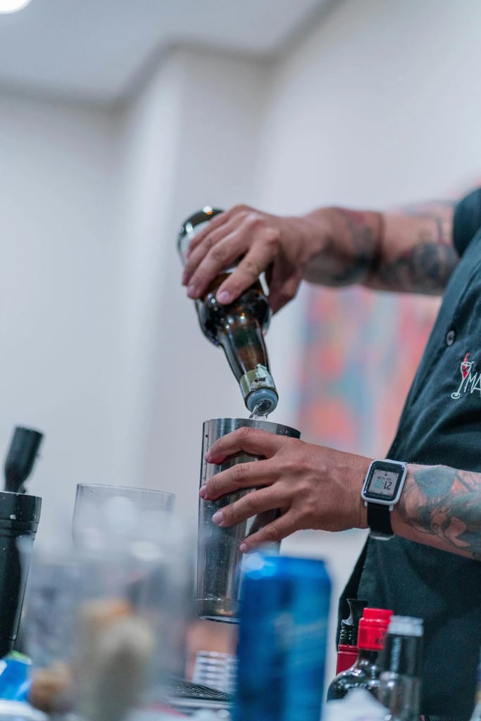 A tattooed male bartender pouring into a cocktail shaker