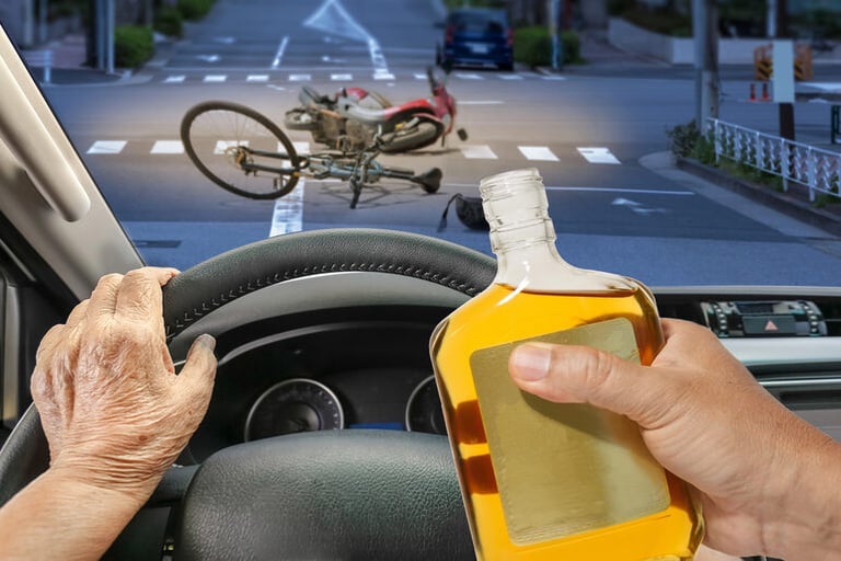 Driver holding a bottle of alcohol behind the wheel as a crashed motorcycle lies ahead on the road, illustrating the dangers of a drunk driver leaving a Spartanburg brewery.