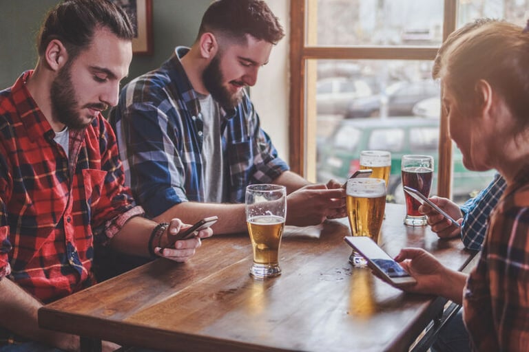 People sitting at a brewery table enjoying craft beer while using smartphones.