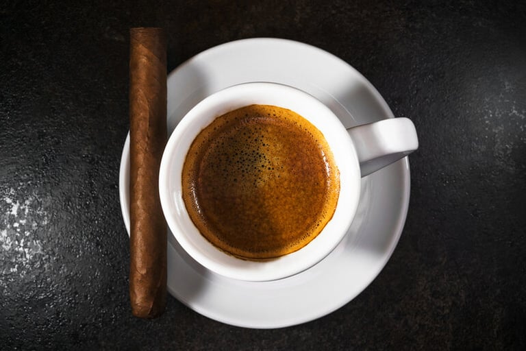 Premium cigar resting beside a cup of coffee on a wooden shelf.