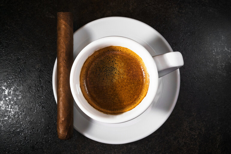 Premium cigar resting beside a cup of coffee on a wooden shelf.