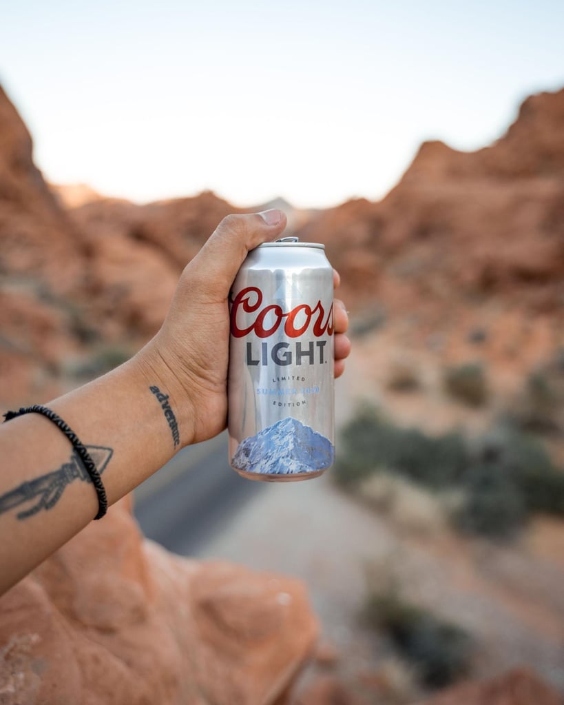 What Are Domestic Beers? Popular American Brands Explained 12 Man with tattooed arm holding a can of Coors Light in the mountains