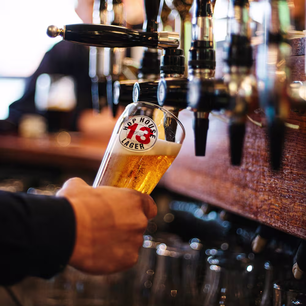 Bartender pouring Hop House 13 Lager from a draft tap into a branded pint glass at a bar.